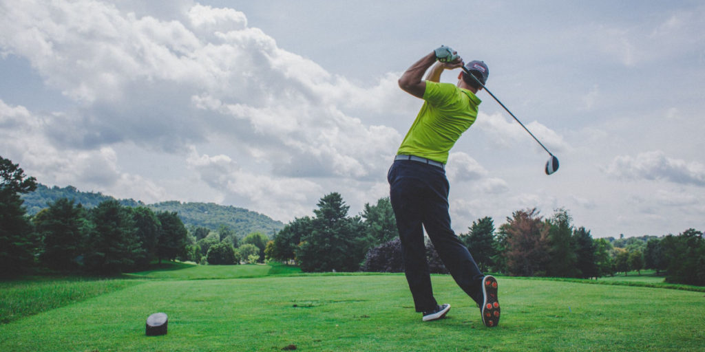 man swinging golf club at tee